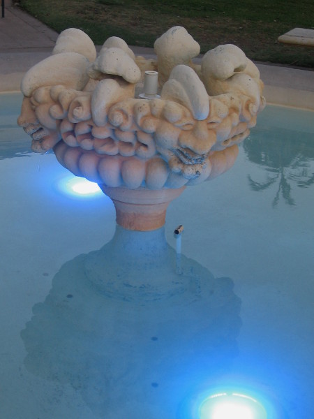 Faces above blue-lit fountain by Botanical Building.